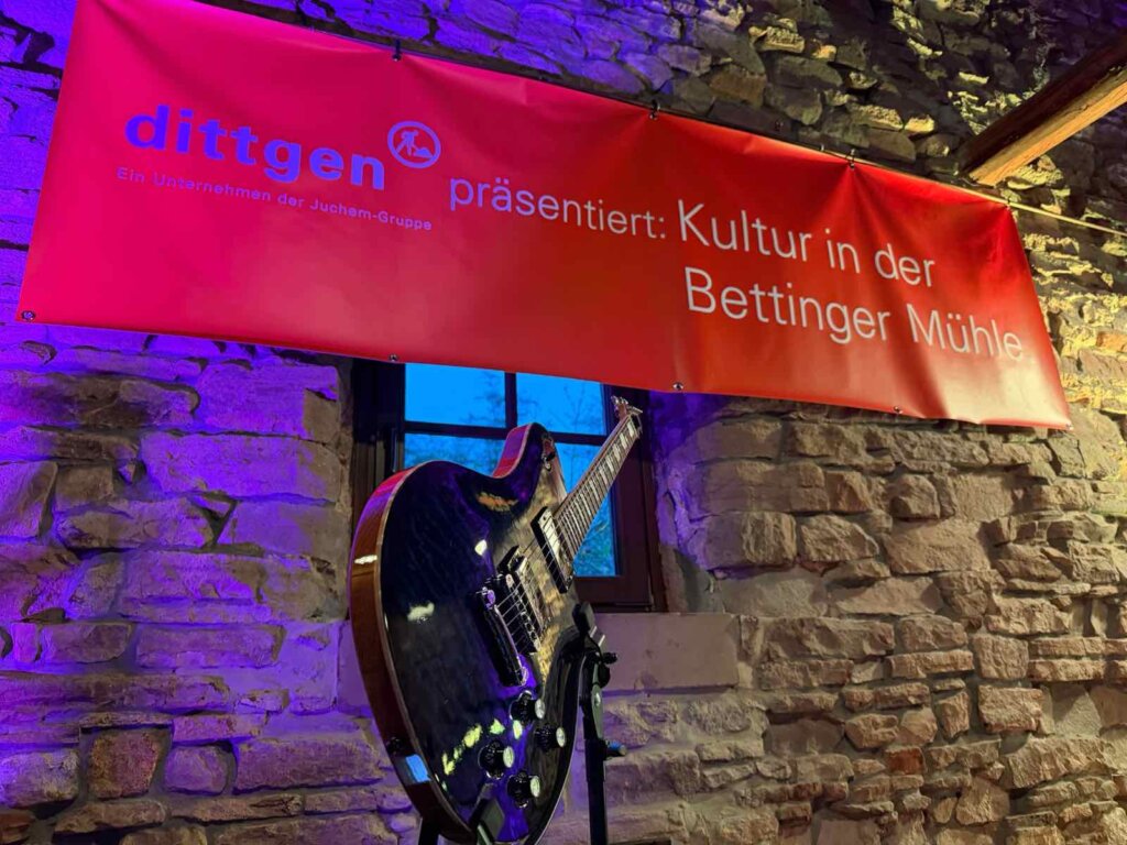 Gitarre vor dem Banner „dittgen präsentiert: Kultur in der Bettinger Mühle“